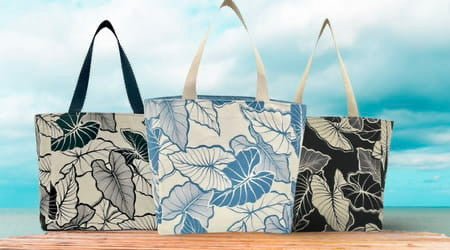 Assortment of three handmade tote bags with distinctive black and white floral patterns, placed on a wooden surface against a serene ocean backdrop, symbolizing sustainable fashion choices.