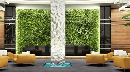 Modern lobby interior with vibrant green living walls, elegant white marble pillar, mustard yellow armchairs, and a tranquil water feature on a blue rug, reflecting eco-friendly luxury design.